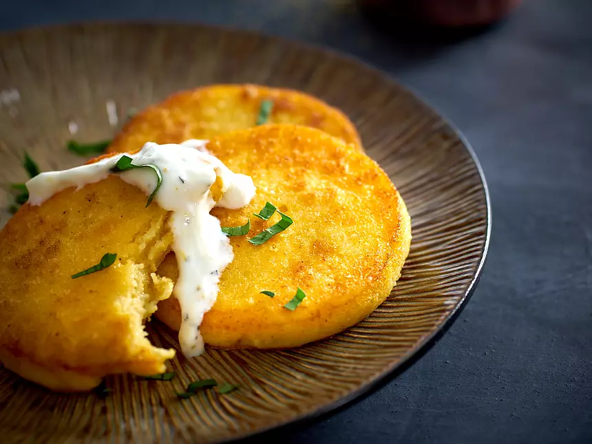 Close-up disks of crispy, golden brown polenta with a drizzle of yogurt sauce.